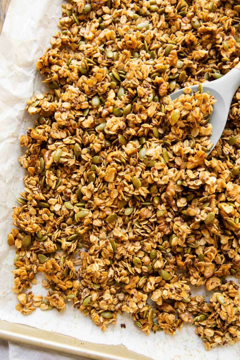 Top shot of Pumpkin Flax Granola on a baking pan with a wooden spoon.