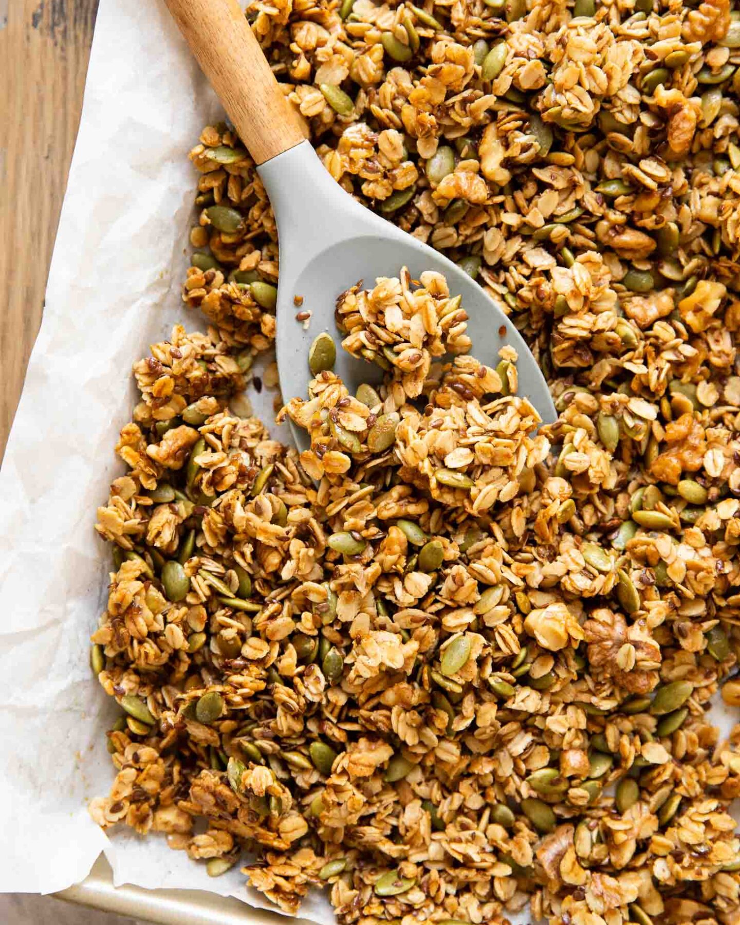 Spoon with pumpkin granola on a baking pan with parchment paper.