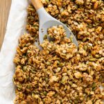 Spoon with pumpkin granola on a baking pan with parchment paper.