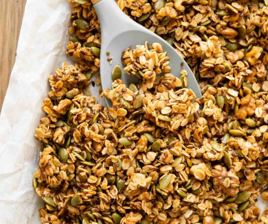 Spoon with pumpkin granola on a baking pan with parchment paper.