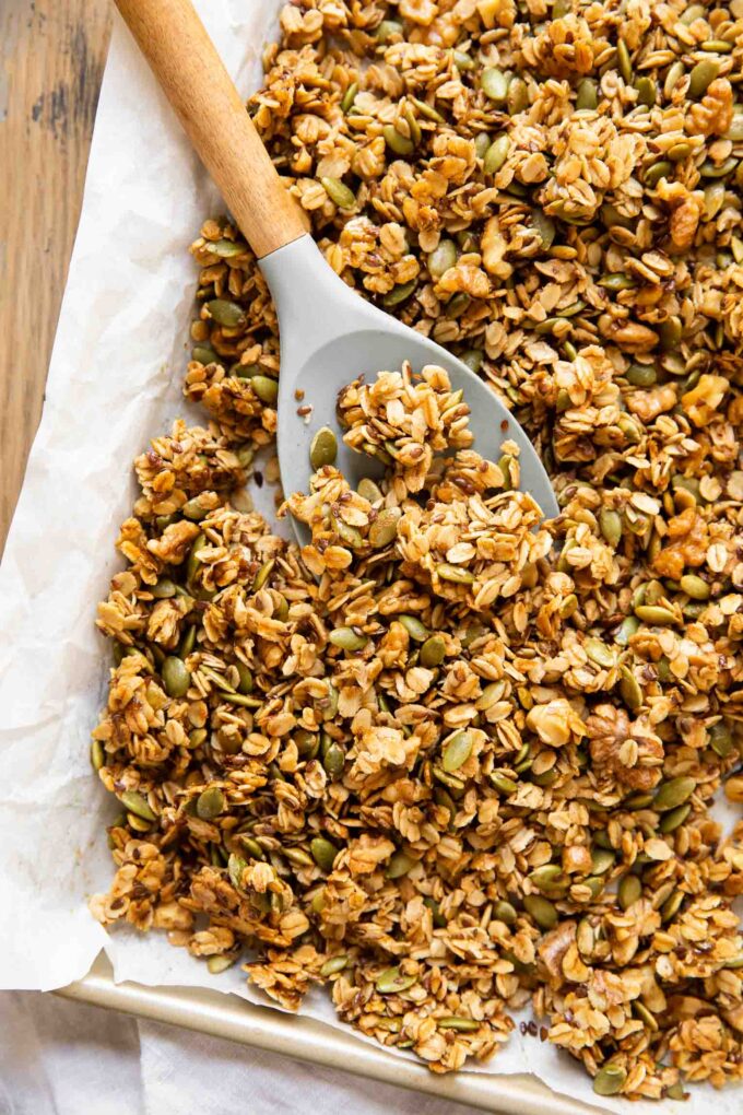 Spoon with pumpkin granola on a baking pan with parchment paper.