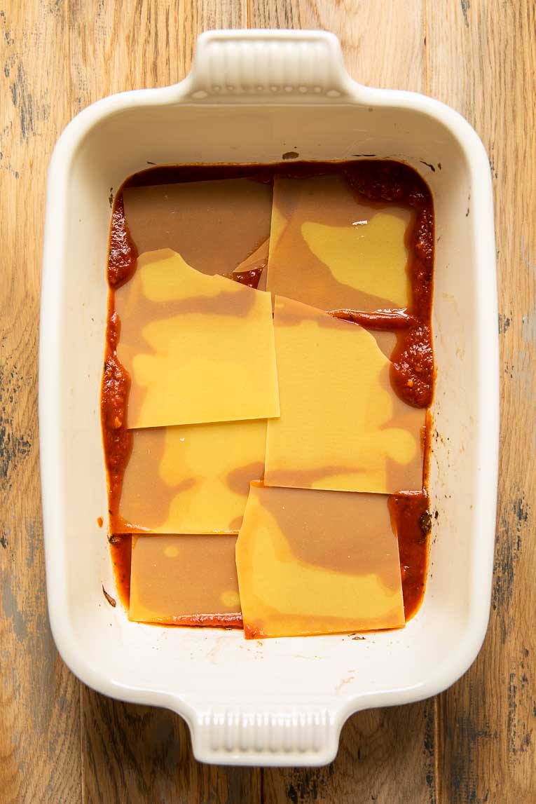 Lasagna noodles with pasta sauce in a casserole dish.