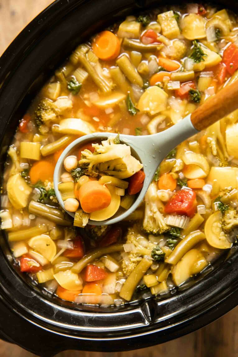 Top shot of vegetable soup in a slow cooker with a spoon.
