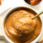 Top shot of spoon removing vegan caramel out of a white bowl.