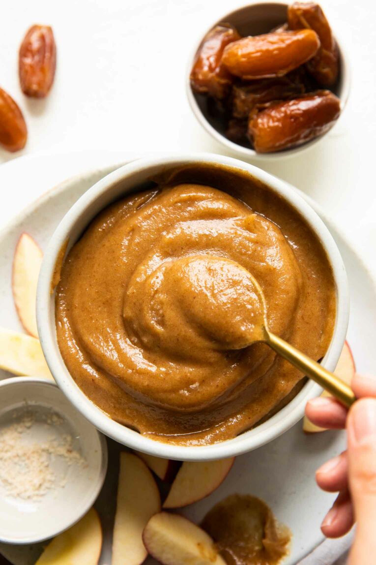 Top shot of spoon in white bowl of vegan caramel sauce.