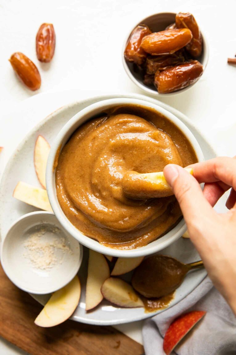 Apples being dipped into vegan caramel sauce.