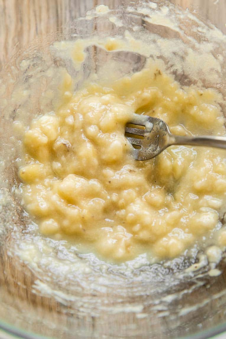 Banana being mashed in a large bowl.
