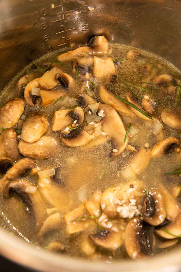 Mushrooms, rice, garlic, onions, and broth in an Instant Pot.