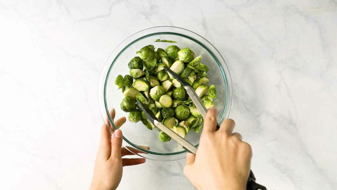 Hands tossing Brussels sprouts in seasoning and oil in a mixing bowl.