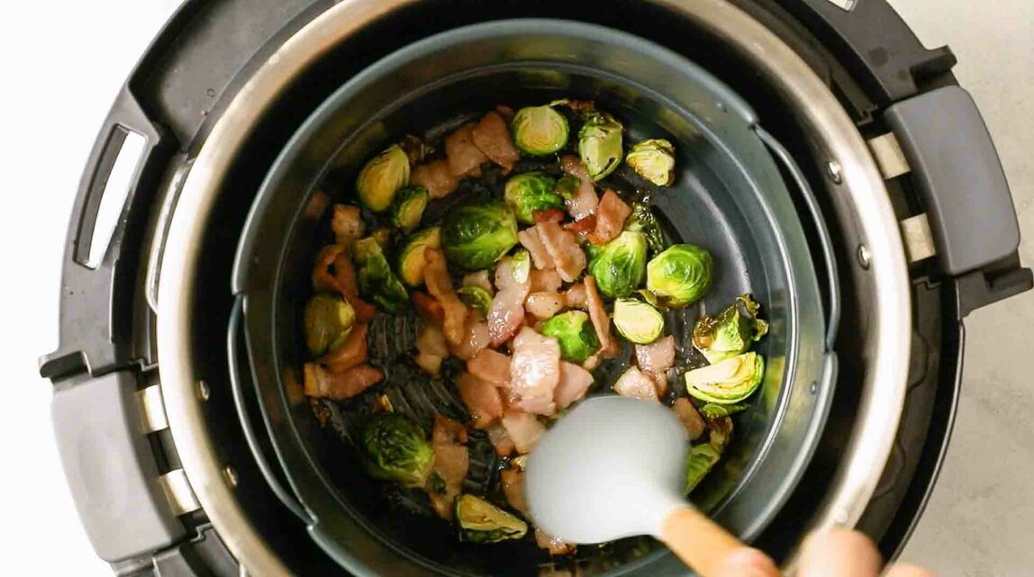 Brussels sprouts and bacon being cooked in an air fryer.