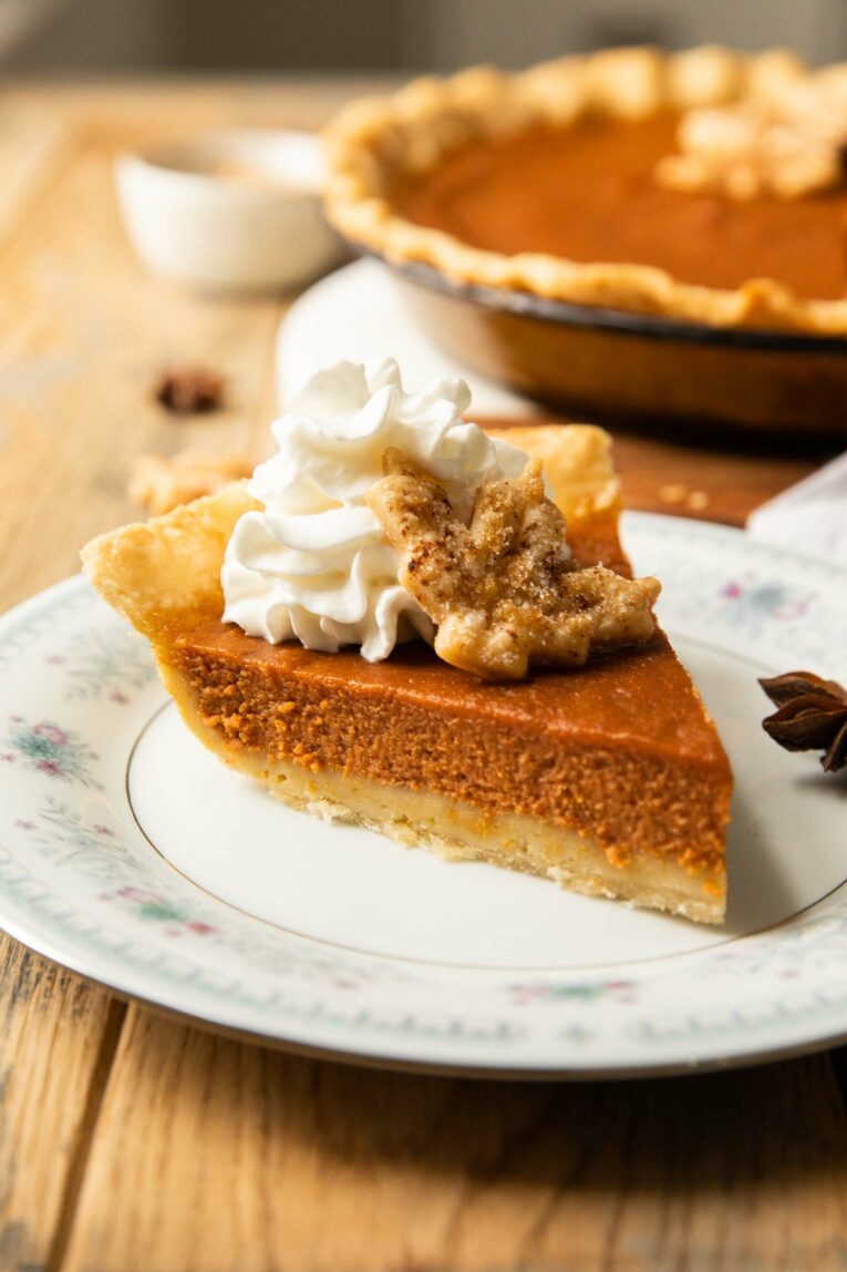 Thanksgiving slice of pumpkin pie with whipped cream and cookie on a plate.