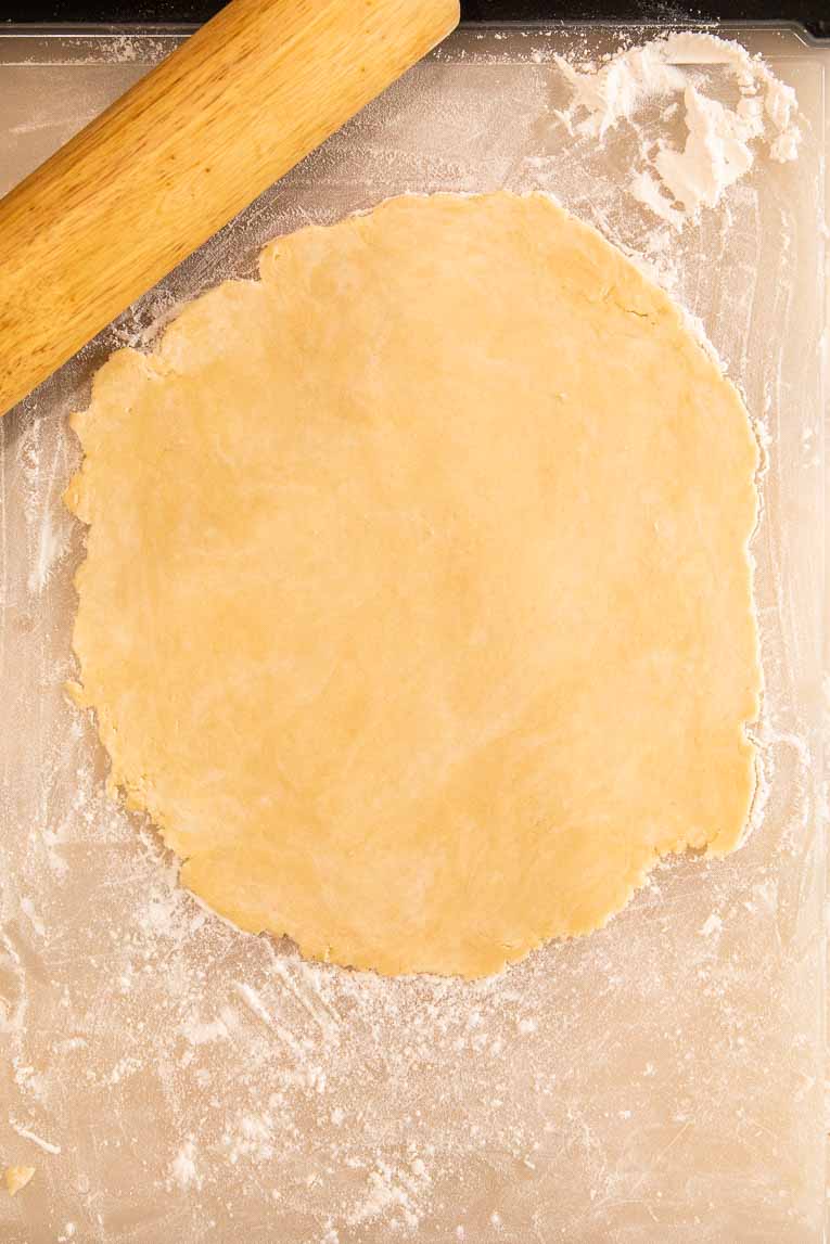 Pie crust being flattened with a rolling pin.