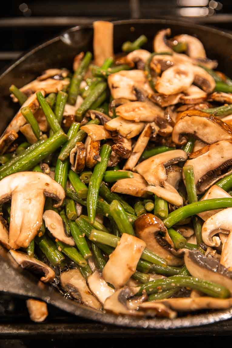 Green beans and mushrooms being sautéed in a skillet.