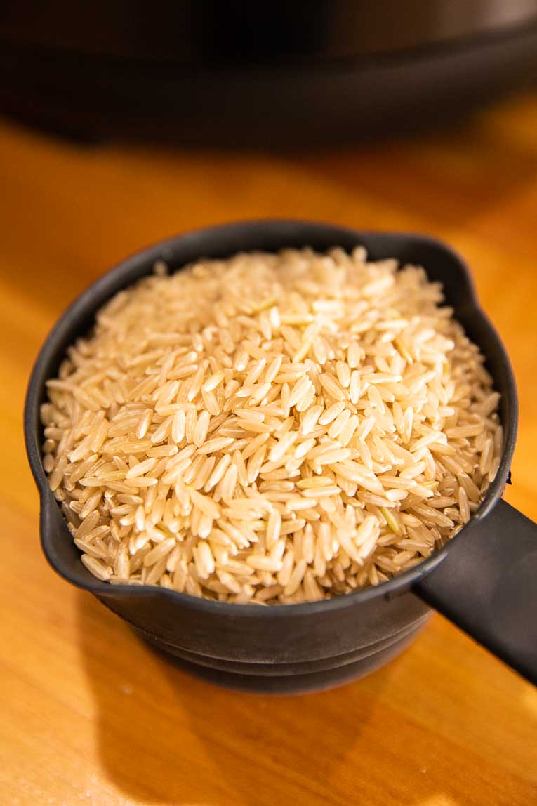 Cup of uncooked brown rice on a countertop.