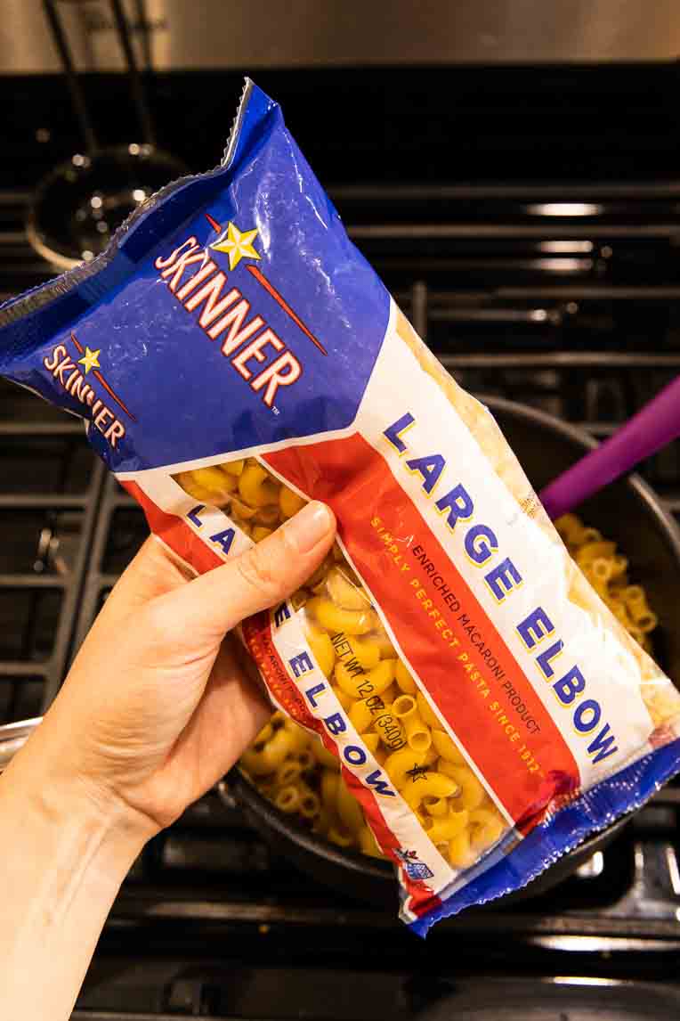 Hand holding Skinner Large Elbows over cooked pasta.