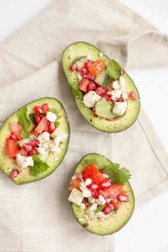 Avocados topped with vegetables and feta cheese.