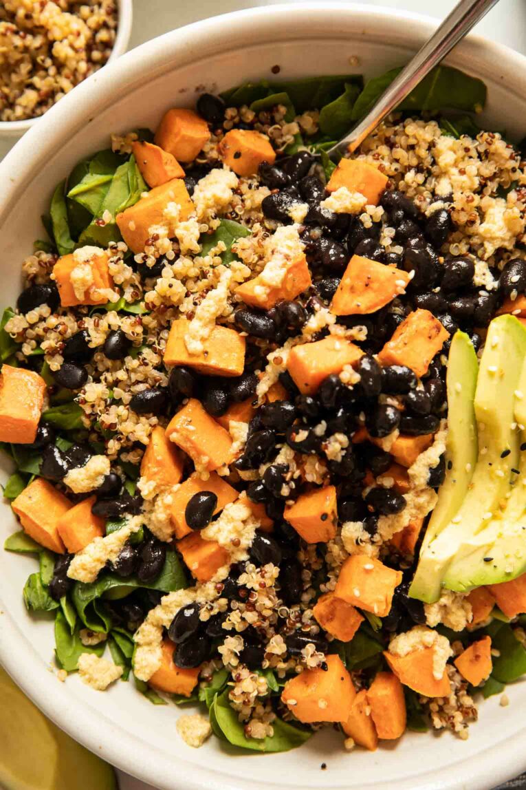 Close up of roasted sweet potatoes, spinach, quinoa, black beans, and avocado.