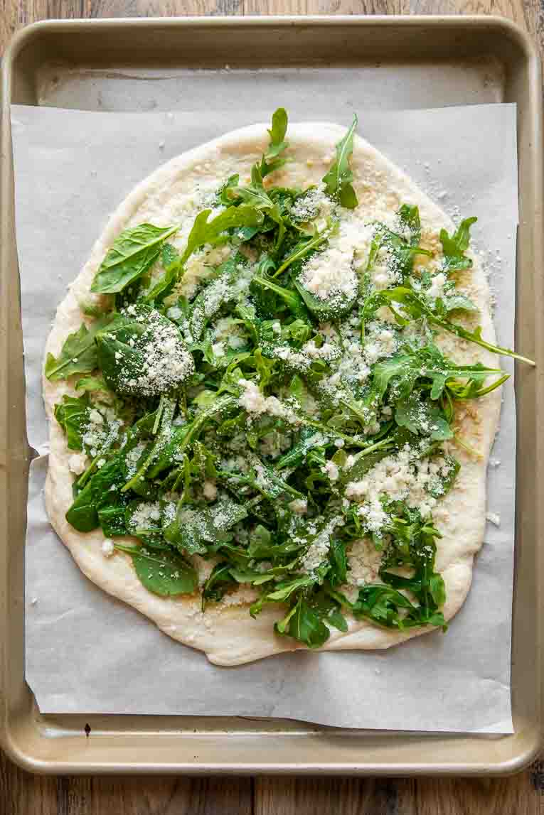 Pizza dough with arugula and parmesan.