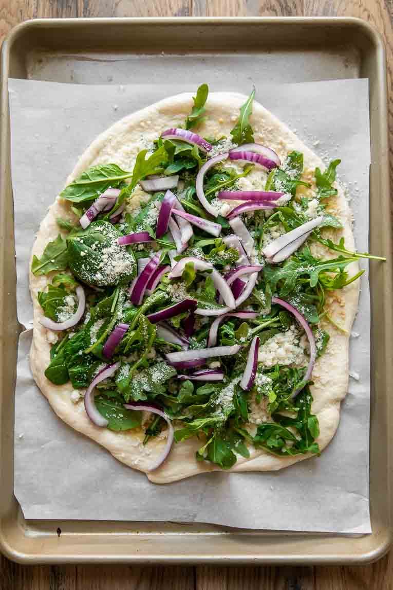 Arugula pizza topped with red onions.