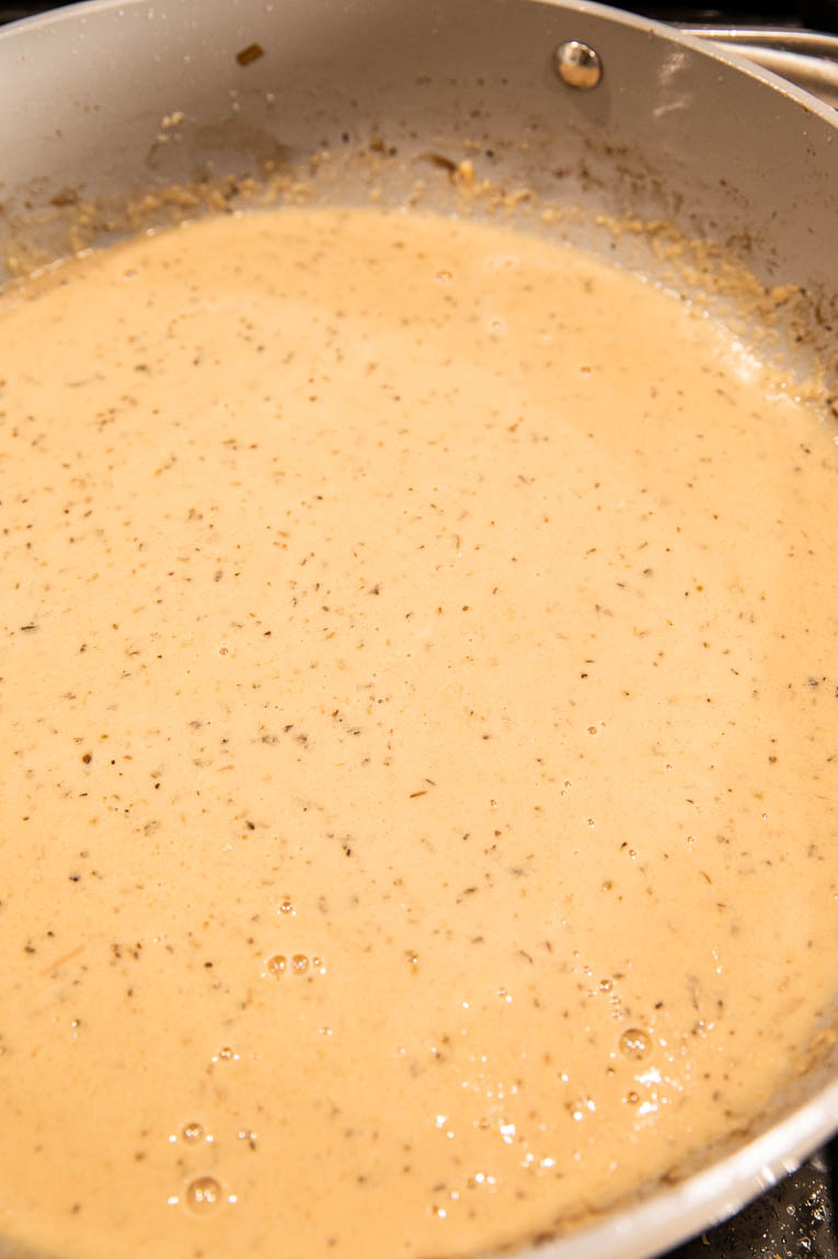Tuscan cream sauce being cooked in a pan.