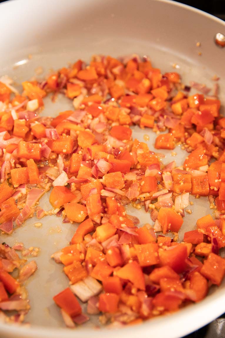 Bell pepper, garlic, and onion being cooked in oil.