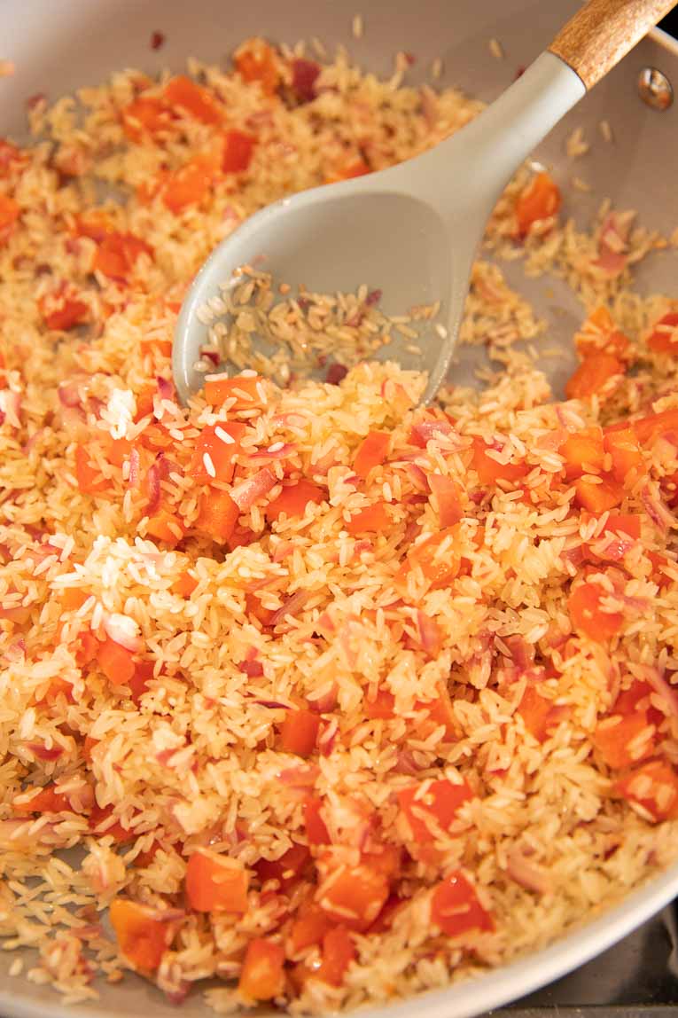 Spanish rice being toasted with garlic, onion, and pepper.