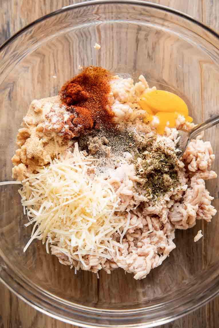 Ground chicken, eggs, parmesan, and spices mixed in a bowl.