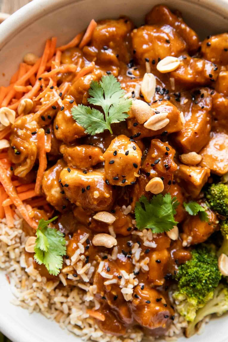 Close up of peanut butter chicken with rice, carrots, broccoli, and sesame seeds.