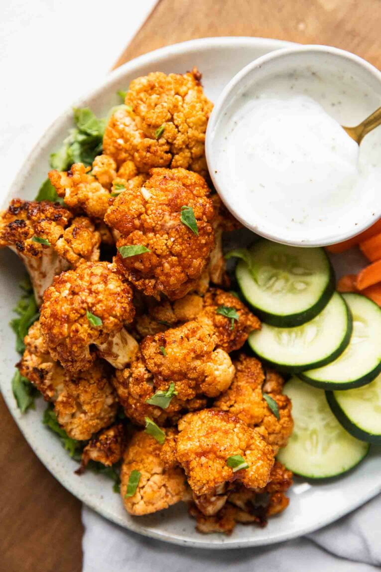 Air Fryer Buffalo Cauliflower Bites on a plate with cucumbers, carrots, and ranch dressing.