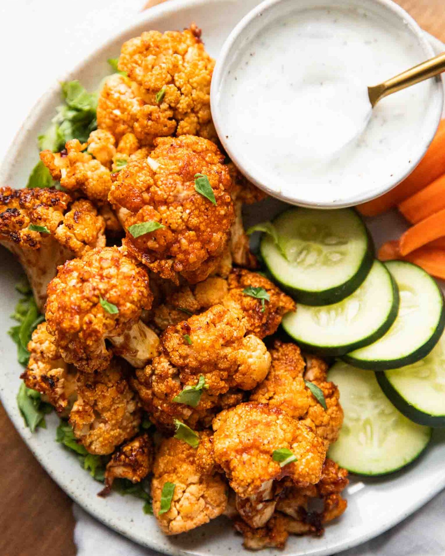 Air Fryer Buffalo Cauliflower Bites on a plate with cucumbers, carrots, and dipping sauce.