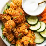 Air Fryer Buffalo Cauliflower Bites on a plate with cucumbers, carrots, and dipping sauce.