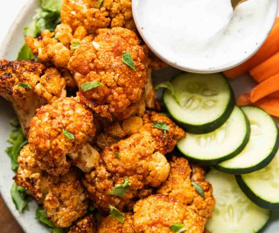 Air Fryer Buffalo Cauliflower Bites on a plate with cucumbers, carrots, and dipping sauce.