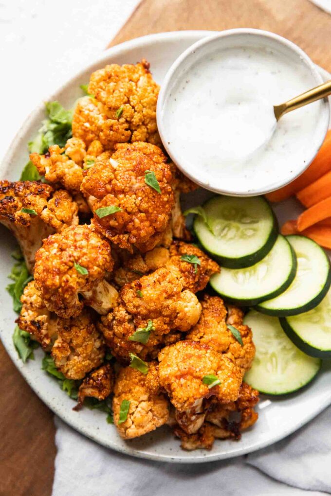 Air Fryer Buffalo Cauliflower Bites on a plate with cucumbers, carrots, and dipping sauce.
