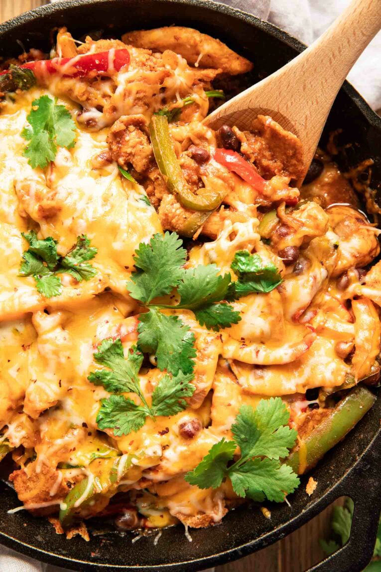 Close up of chicken fajita casserole recipe in a cast iron skillet with a spoon.