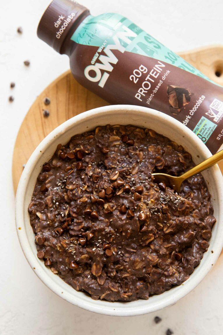 Bowl of chocolate protein oats next to dark chocolate protein shake.