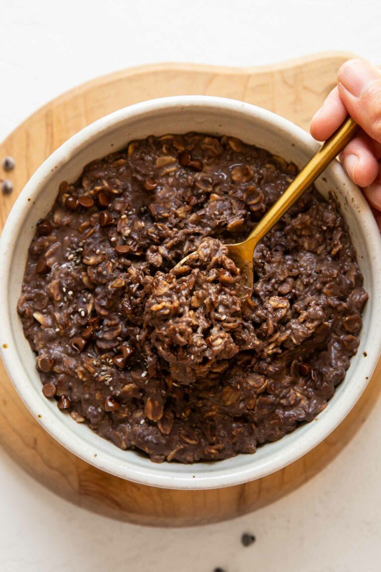 Hand scooping spoon of protein oatmeal from a bowl.