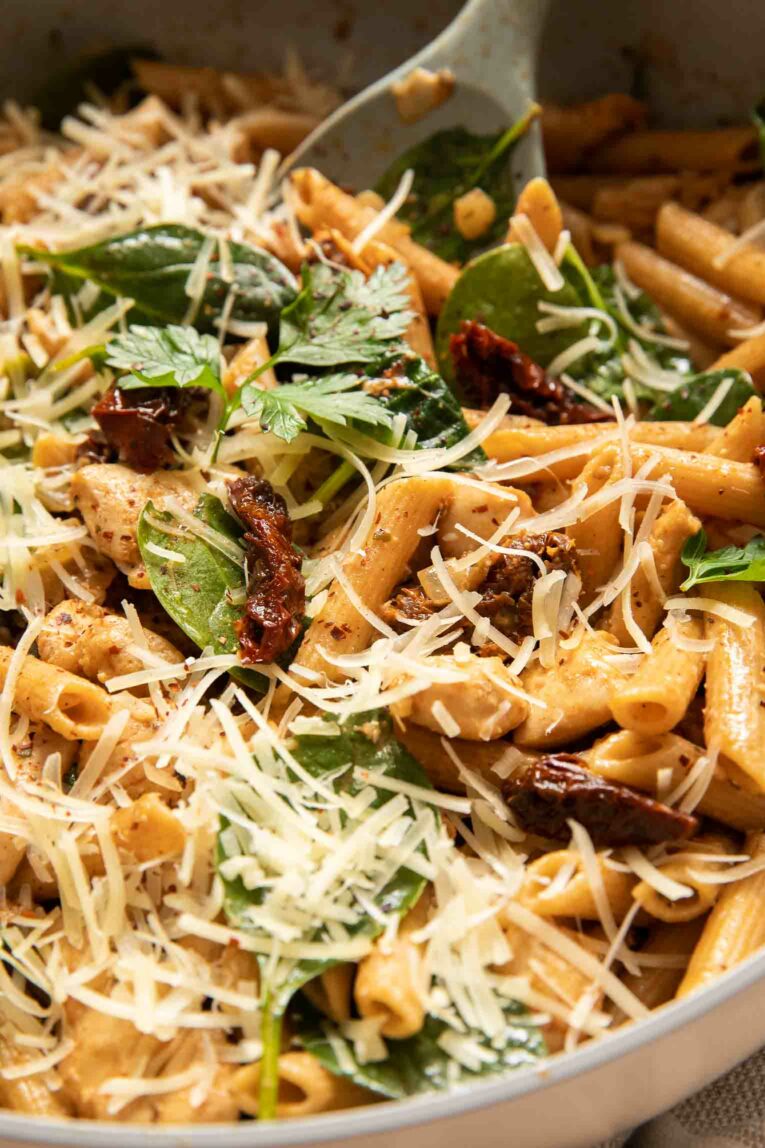 Angled photo of sun-dried tomato chicken pasta in a skillet.