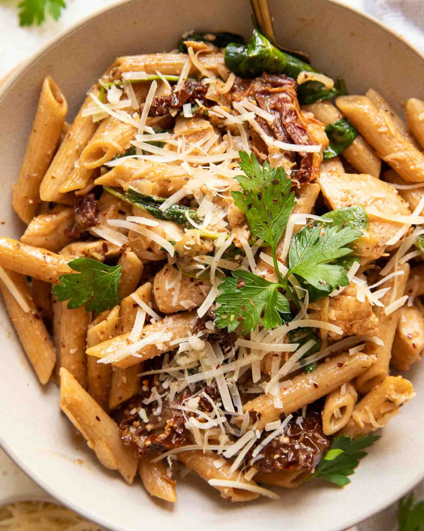 Parmesan sun-dried tomato chicken pasta in a white bowl with a fork.