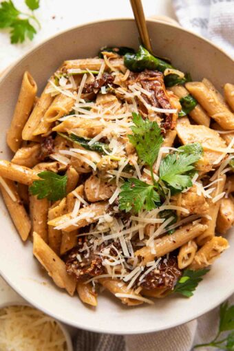 Parmesan sun-dried tomato chicken pasta in a white bowl with a fork.