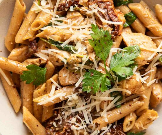 Parmesan sun-dried tomato chicken pasta in a white bowl with a fork.