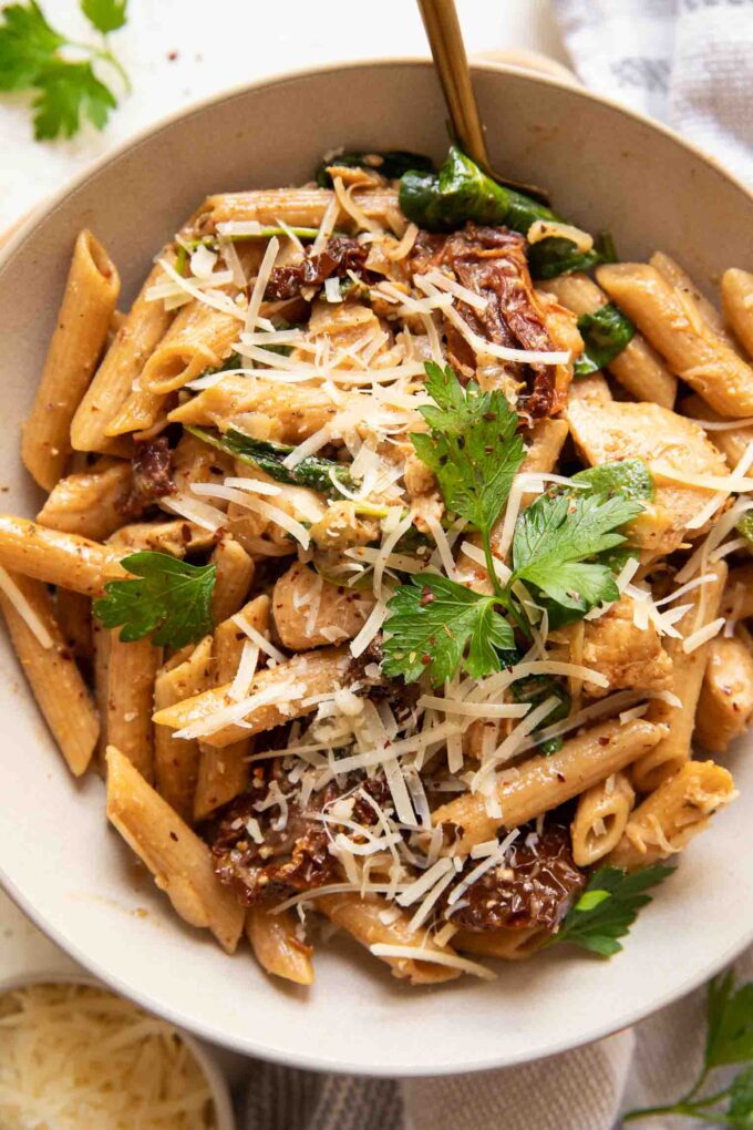 Parmesan sun-dried tomato chicken pasta in a white bowl with a fork.