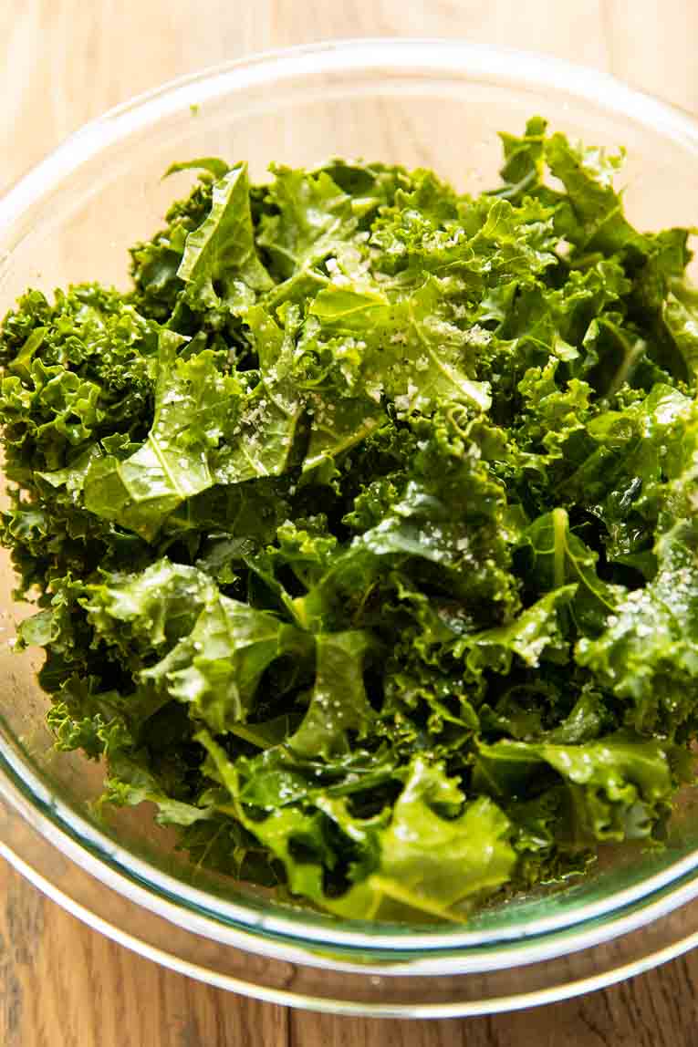 Kale with olive oil, salt, and pepper in a glass bowl.