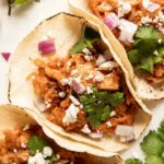 Close up of jackfruit pulled pork tacos with cilantro, cotija cheese, and onions.