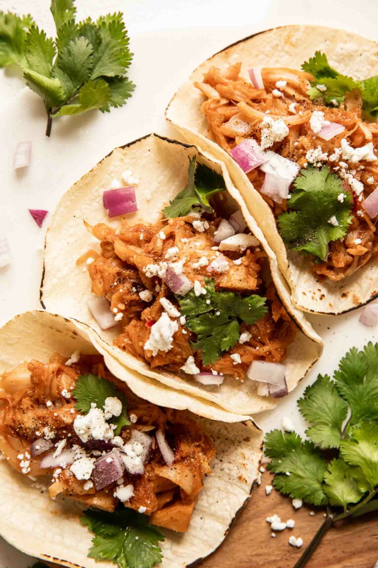 Vegetarian jackfruit tacos with toppings on corn tortillas.