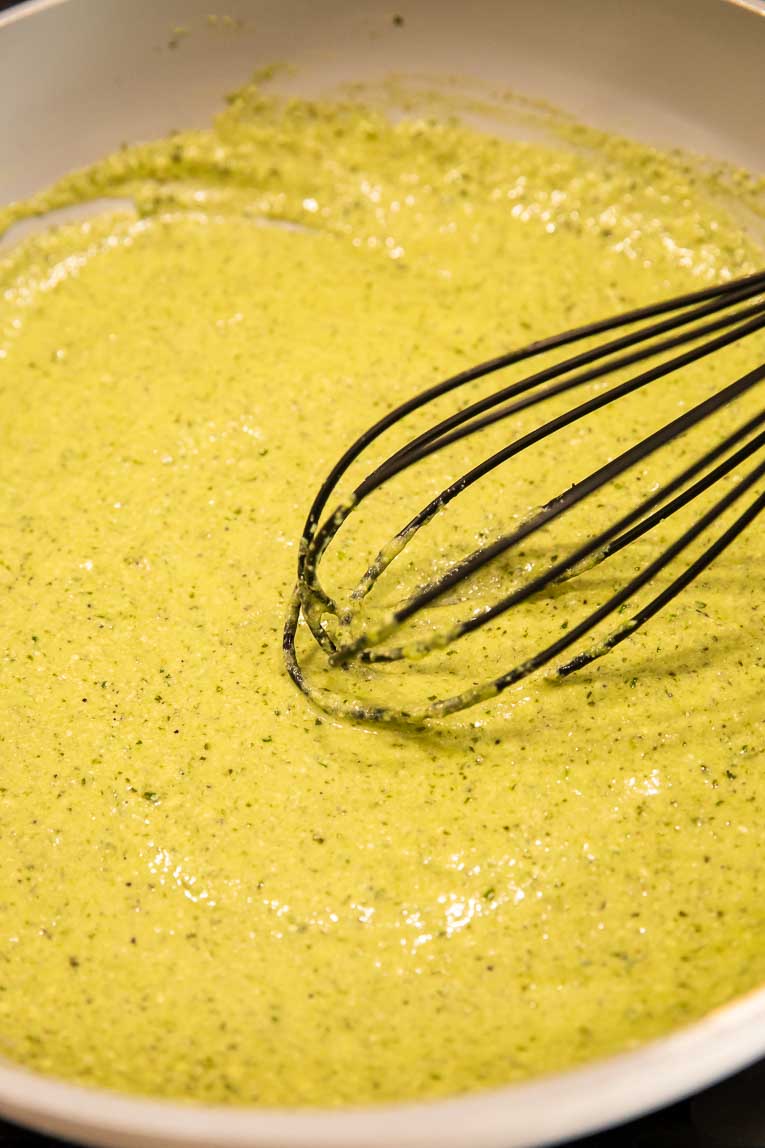 Pesto sauce being whisked in a pan.