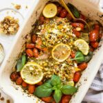 Baked pesto salmon in a casserole dish with tomatoes and basil.
