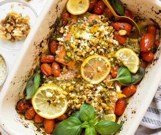 Baked pesto salmon in a casserole dish with tomatoes and basil.