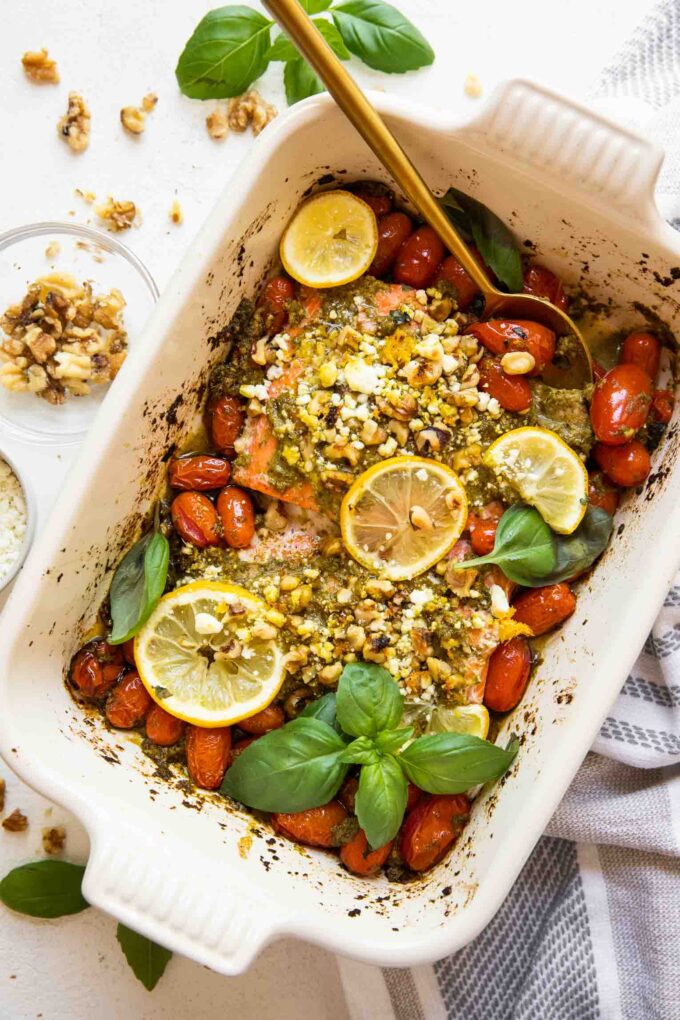 Baked pesto salmon in a casserole dish with tomatoes and basil.