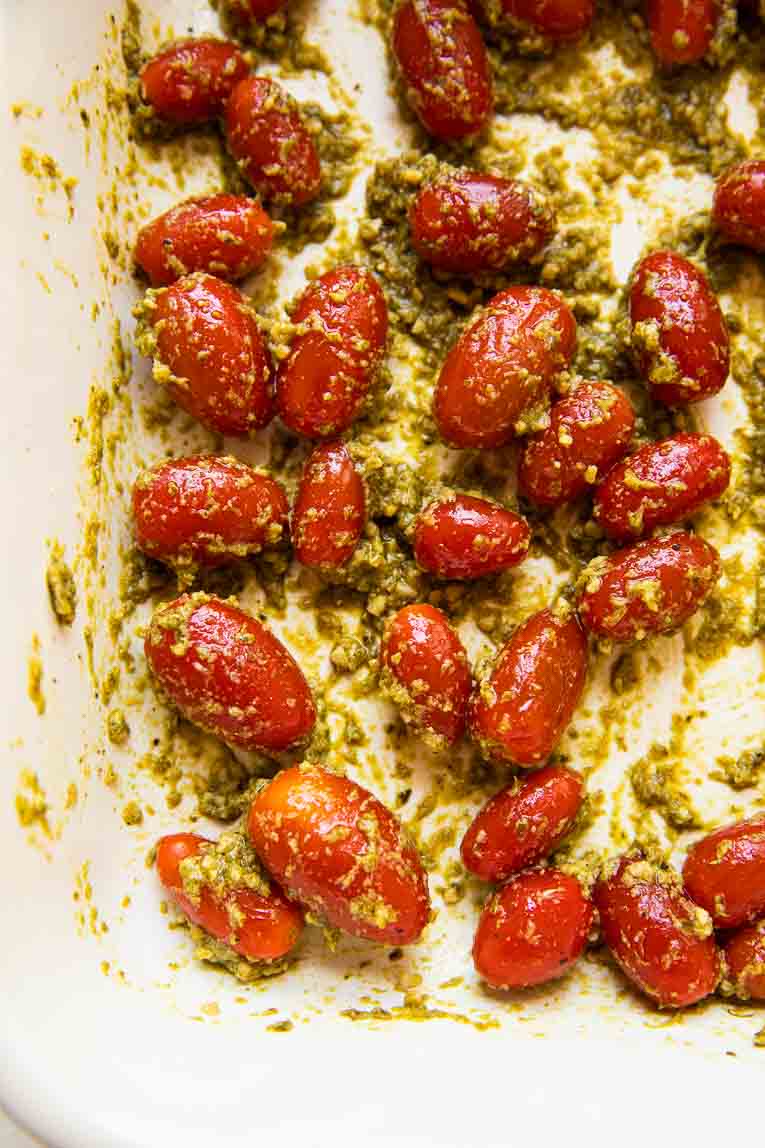 Tomatoes and pesto being roasted in a baking dish.