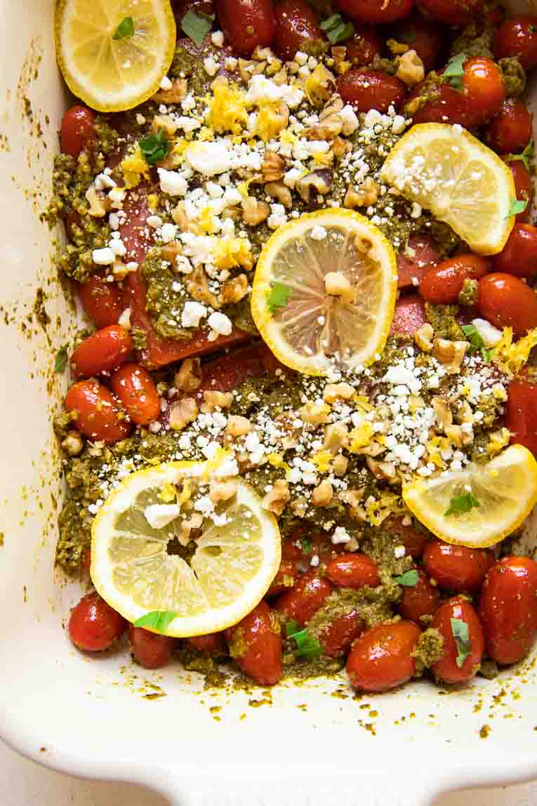 Salmon filets, tomatoes, pesto, lemon, and goat cheese in a baking dish.